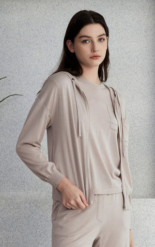 Light gray zip knit cardigan with hood and front pockets; layered top peeks at hem.