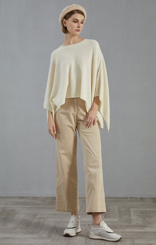 White cashmere poncho sweater with relaxed drape and wide arm openings, worn with pants