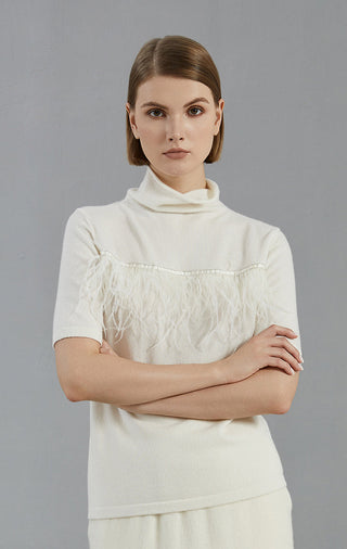 White high-neck short-sleeve sweater with fringe band across chest, arms crossed
