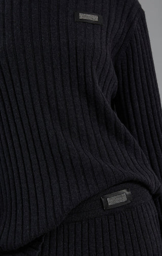 Close-up of dark charcoal ribbed sweater with rectangular beaded logo label