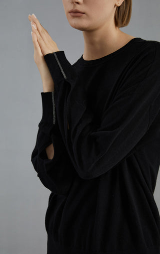 Black wool knit sweater close-up: round neck and ribbed cuffs on relaxed sleeves