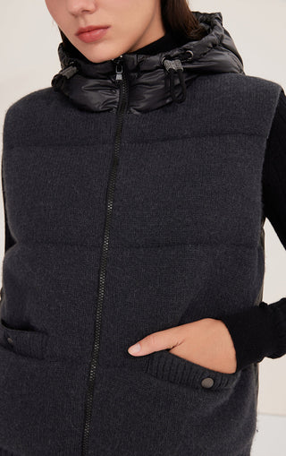 Black hooded down vest close-up: full-zip front, drawstring hood, buttoned pocket