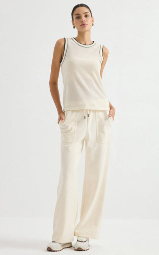 Cream sleeveless cashmere knit top with dark contrast trim, worn with light pants
