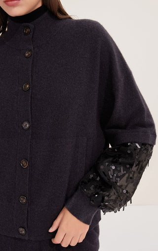Close-up: black knit cardigan placket with metal buttons and embellished sleeve cuff.