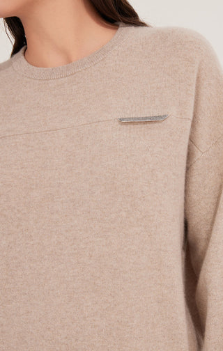 Close-up of camel cashmere knit top: chest shimmer accent tab and ribbed crew neckline.