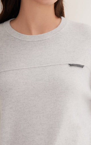 Close-up of light gray cashmere knit top with shimmer accent tab near the neckline.