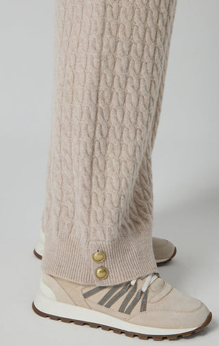 Camel cable-knit pants with ribbed ankle cuff and wide-leg drape over sneakers.