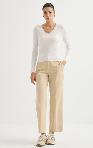 White ribbed wool V-neck sweater, long sleeves, worn with light pants.