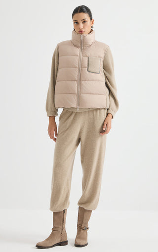 Camel cashmere puffer vest with zip front and flap chest pocket, paired with track pants.