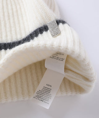 Cream cashmere beanie with black stripe cuff and silver stitch badge.