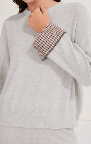 Light gray sweater close-up: checked cuff trim at wrist with small buttoned edge