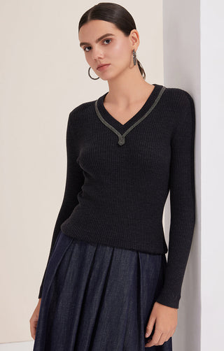 Black ribbed wool V-neck sweater with beaded trim, paired with a pleated skirt