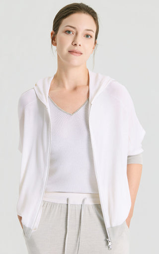 White hooded knit cardigan with front zipper and drawstring hood; layered over knit top