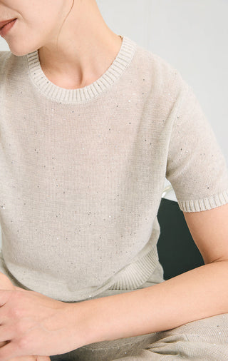 Close-up of light gray sequin knit short-sleeve top at crew neck and ribbed hem