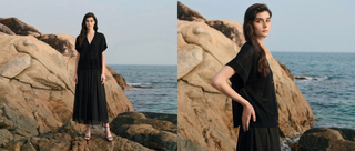 Model wearing a black women’s summer outfit by a rocky coastline with ocean background