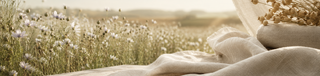 Natural linen fabrics arranged in a sunlit flax field, highlighting breathable texture, airy softness, and refined summer comfort.