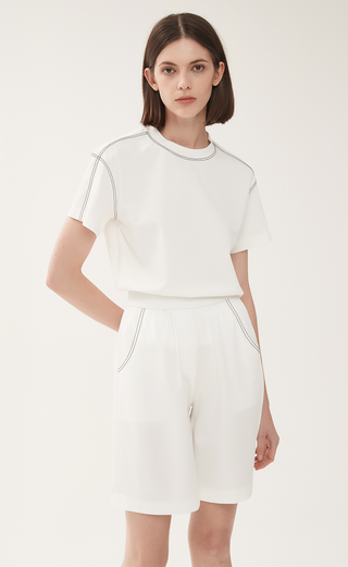 White shorts with elastic waistband, side pockets, and contrast stitched trim at hem