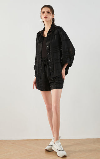 Black silk textured drawstring shorts on model, elastic waist and patch pockets
