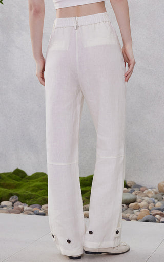 White linen straight-leg pants with wide cuffs and button detail at hem
