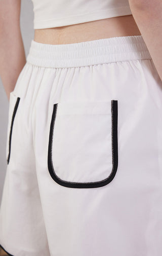 White elastic-waist shorts close-up: U-shaped black-trim pocket