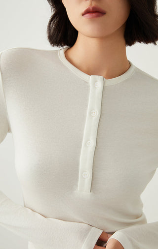 White henley neckline close-up with button placket and small collar tab.