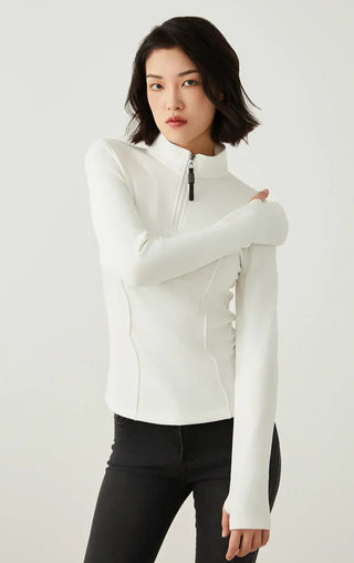 White half-zip knit top with high neck and beaded zipper pull, arms crossed