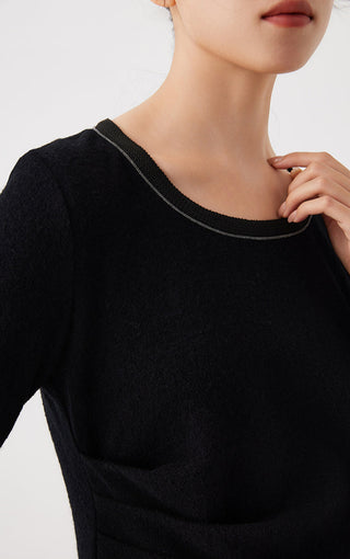Close-up of black crew-neck top with fine beaded trim around neckline and long sleeve