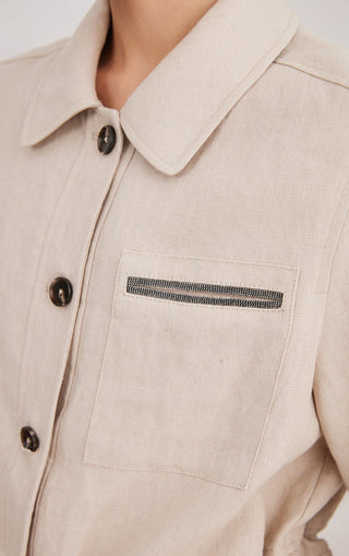 Beige linen utility shirt close-up: button collar, chest pocket with beaded trim