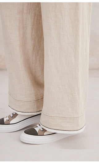 Beige linen trousers hem with wide leg opening and cuffs above sneakers