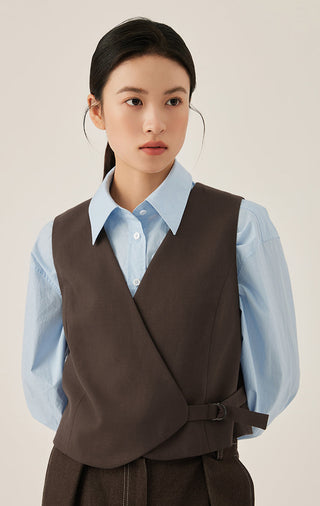 Dark brown wrap vest worn over a light blue button shirt; tie belt at waist