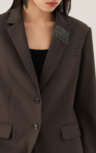 Dark brown blazer lapel close-up with shimmer fringe detail and button