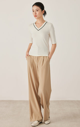 White V-neck top with black trim and short sleeves, worn with beige trousers