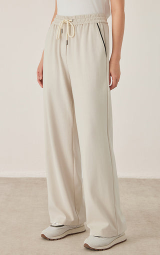 Cream wide-leg pants with drawstring and side pocket detail, relaxed ankle-length