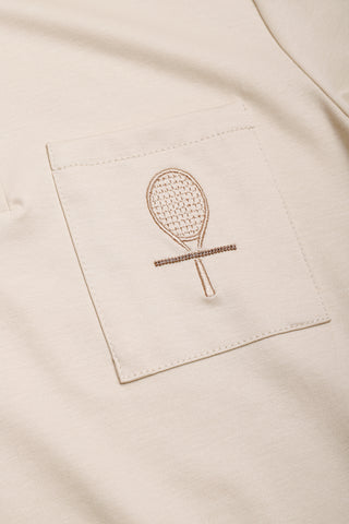 Close-up of embroidered racket logo on camel chest pocket of polo dress.