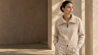 Woman wearing an ivory ribbed zip cardigan in a sunlit stone interior